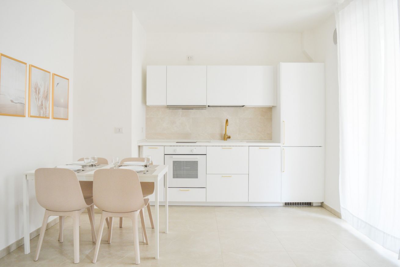 Una cocina moderna con armarios blancos, una isla central y un comedor con sillas.