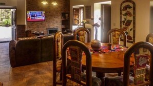Zona pranzo con un tavolo rotondo in legno, sedie decorate, una televisione e un camino.