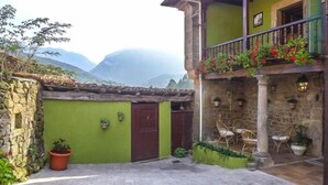 Un cortile con un muro in pietra, una porta verde e un balcone con mobili in vimini.