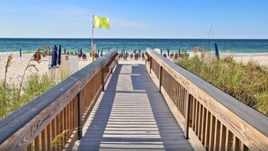 A wooden boardwalk leading to a beach with umbrellas and lounge chairs. - Crystal Tower 908 | Gulf Shores Beachfront | 3 Pools, Hot Tub, Lazy River (Gulf Shores)