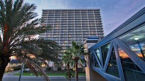 A high-rise hotel with a modern glass facade, multiple balconies, and a palm tree-lined entrance. - Crystal Tower 908 | Gulf Shores Beachfront | 3 Pools, Hot Tub, Lazy River (Gulf Shores)