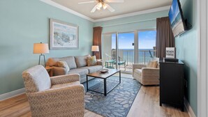 A living room with a sofa, armchairs, a coffee table, a TV, and a ceiling fan. - Crystal Tower 908 | Gulf Shores Beachfront | 3 Pools, Hot Tub, Lazy River (Gulf Shores)