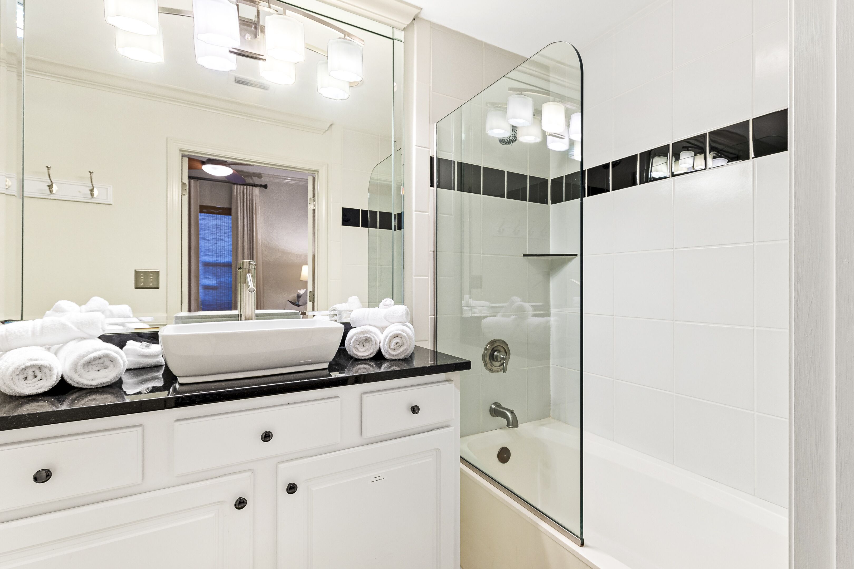 Une salle de bain moderne avec une douche à parois de verre, un grand miroir et un plan de toilette noir agrémenté de serviettes blanches.