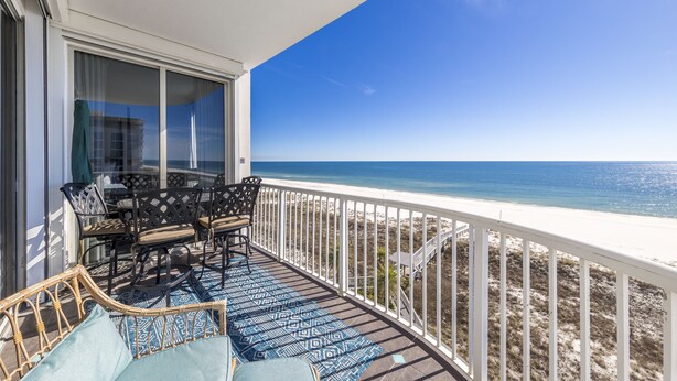 Ein Balkon mit Blick auf den Strand, ein Tisch mit Stühlen und eine Rattan-Couch.