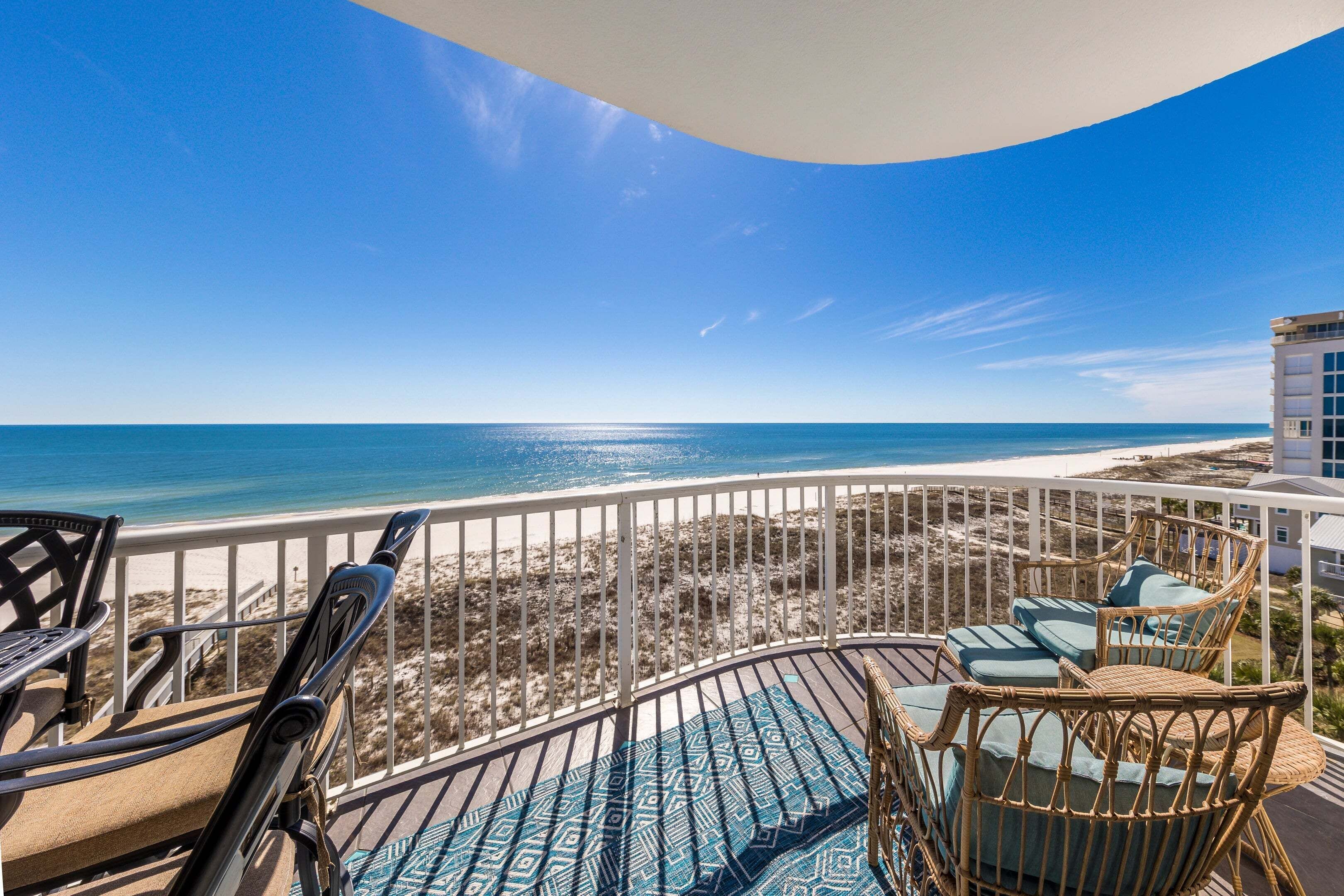 A balcony with wicker furniture overlooking a beach.