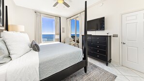 Ein Schlafzimmer mit Bett, Deckenventilator, Fernseher, Kommode und Blick auf den Ozean.
