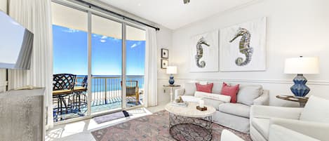 Un salon spacieux avec un balcon donnant sur la mer, un ventilateur de plafond et un canapé agrémenté de coussins décoratifs.