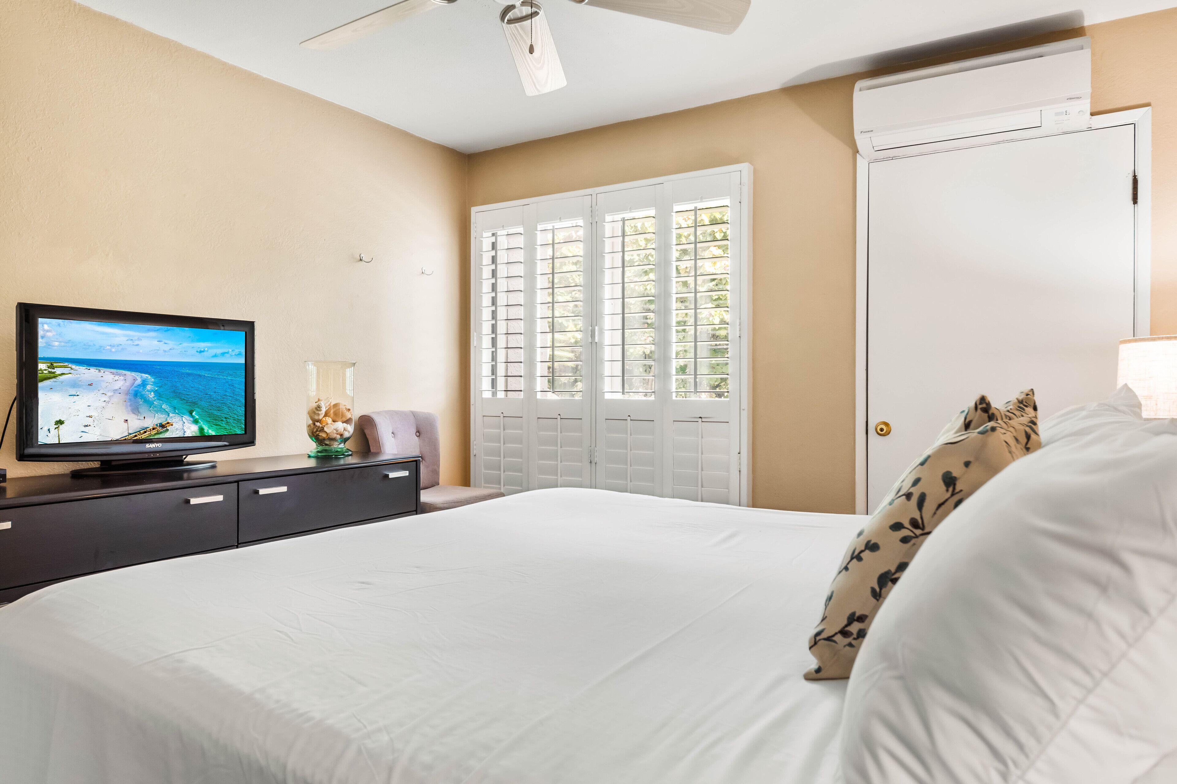 Ein Schlafzimmer mit einem Bett, einem Fernseher auf einer Kommode, einem Kleiderschrank und einem Fenster mit Fensterläden.