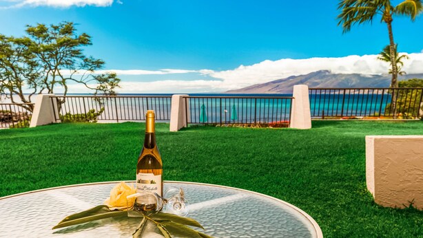 Ein Tisch mit einer Weinflasche, einem Glas und einer Blume, mit Blick auf Strand und Berge.