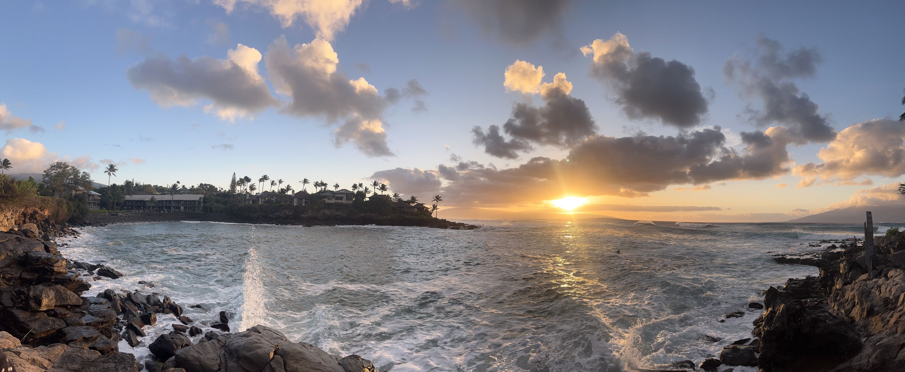 A coastal scene with rocky shores, ocean waves, and a sunset.