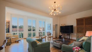 Un salon spacieux doté d’une grande fenêtre, d’un téléviseur à écran plat et d’un lustre moderne.