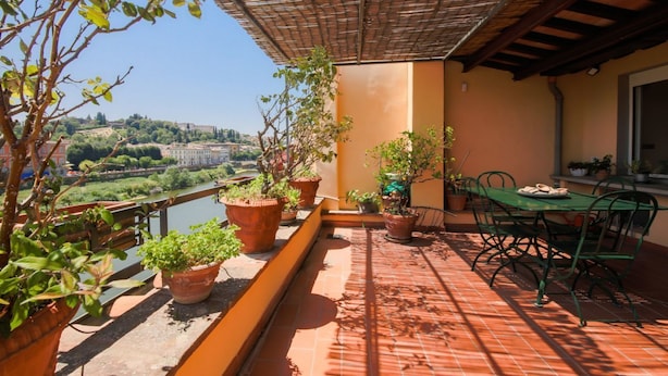 Un balcon agrémenté de plantes en pot, une table avec des chaises et une vue sur une rivière et des bâtiments.