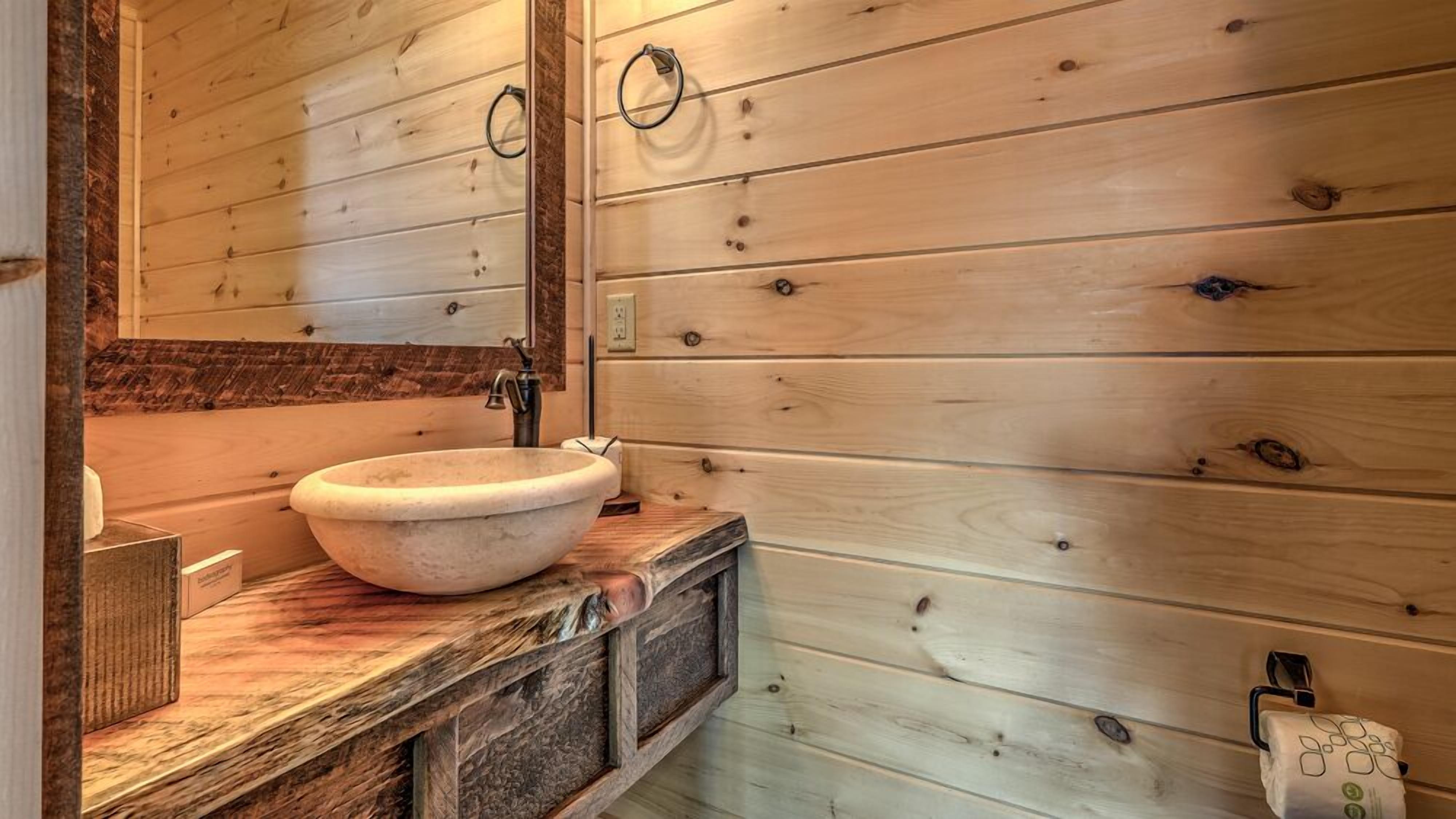 Un baño de cabaña de madera con un lavabo de piedra, armarios de madera y un espejo.