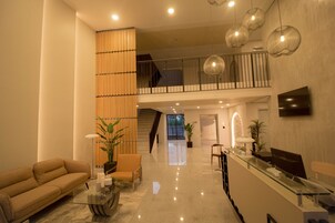 A spacious lobby with a high ceiling, a reception desk, a sofa, and a staircase leading to an upper level.