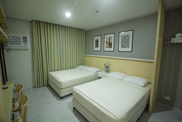 Habitación de hotel con dos camas, un escritorio, sillas y una ventana con cortinas.