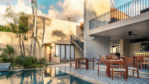 A modern pool area with a checkered floor, wooden furniture, and a staircase leading to a balcony.