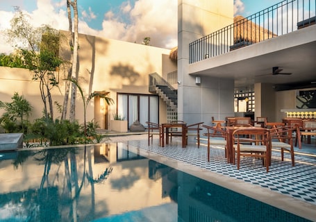 A modern pool area with a checkered floor, wooden furniture, and a staircase leading to a balcony.