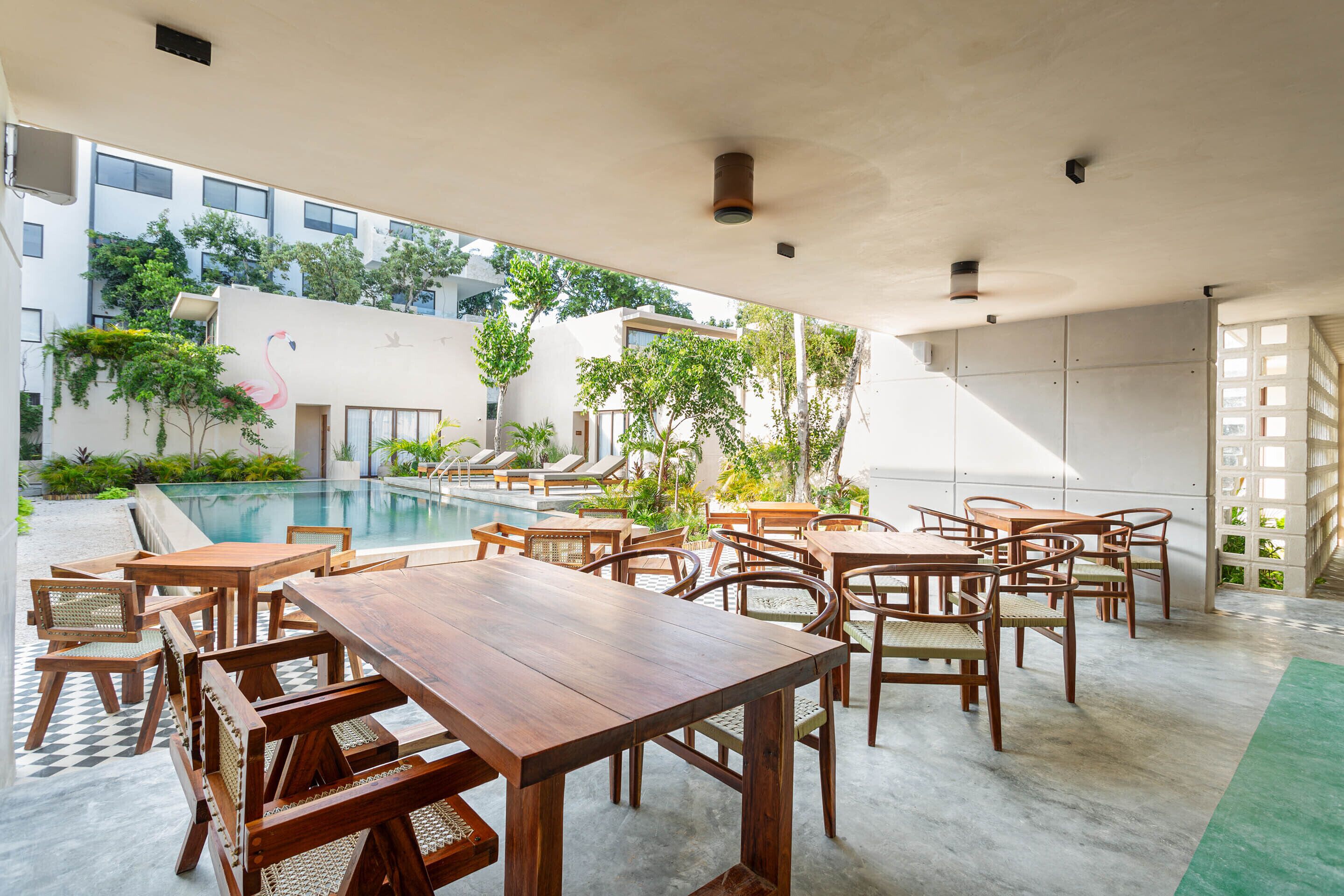 A poolside area with wooden tables and chairs, a pool, and a view of a building with a pink flamingo mural.