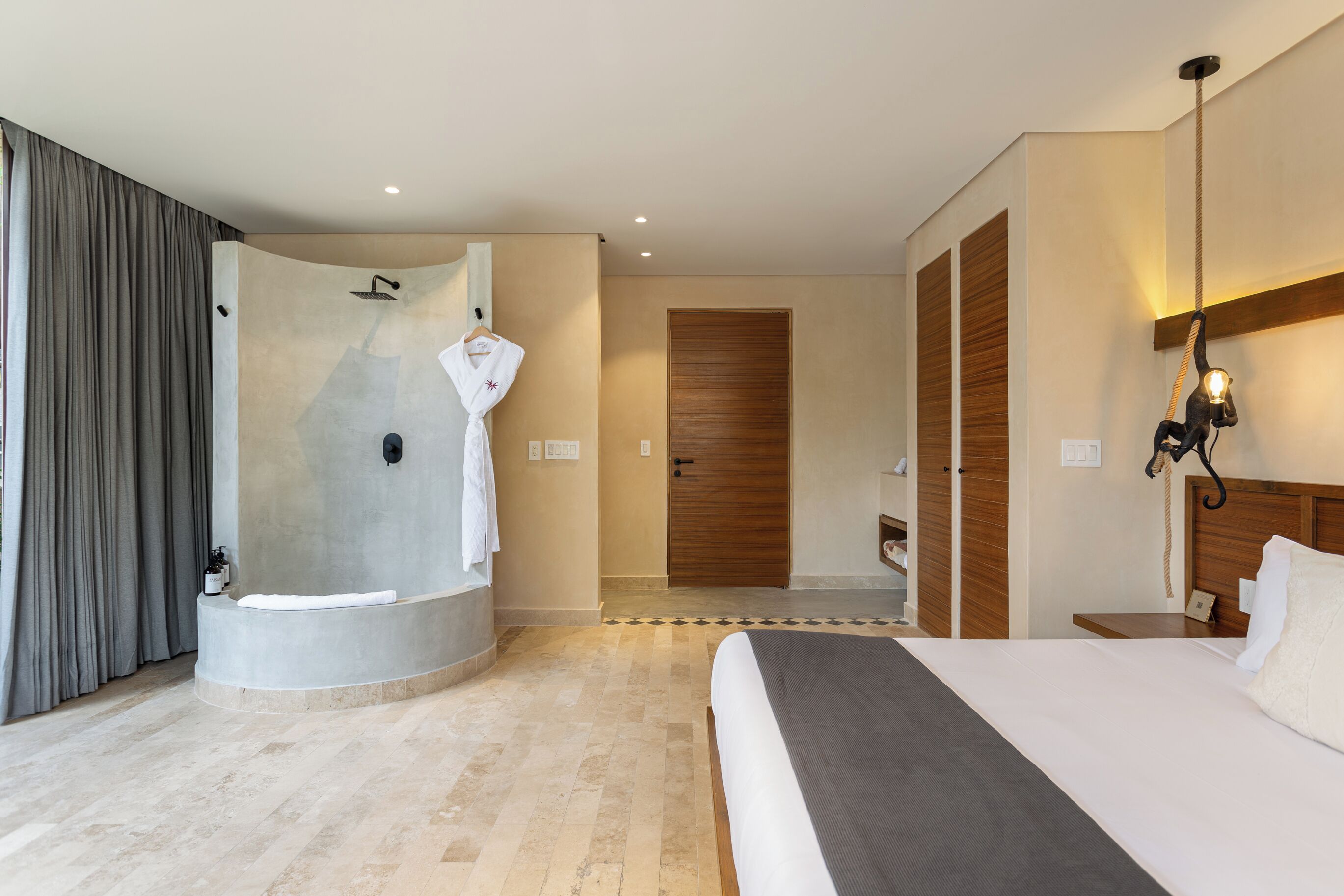 A modern hotel room with a large bed, a walk-in shower, and a wooden door.