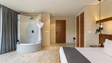 A modern hotel room with a large bed, a walk-in shower, and a wooden door.