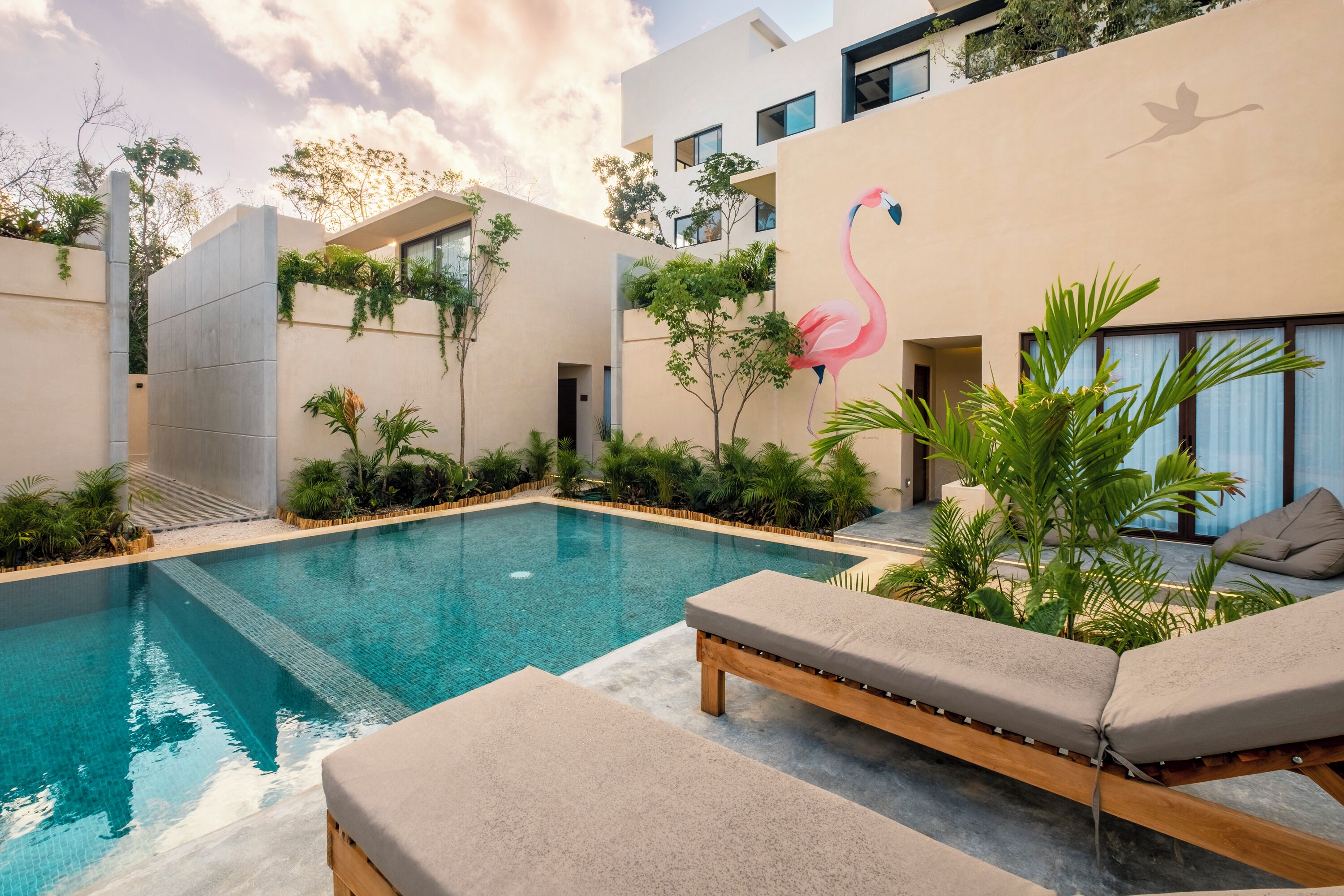 A modern pool area with lounge chairs, a swimming pool, and a building with a large flamingo mural.