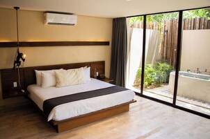 A bedroom with a large bed, a wooden headboard, a bedside table, a nightstand, a wall-mounted air conditioner, and a view of a garden through a sliding glass door.