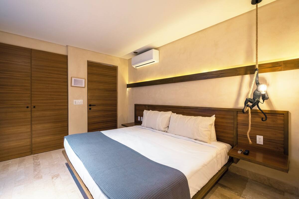 A hotel room with a large bed, wooden wardrobe, and an air conditioning unit.