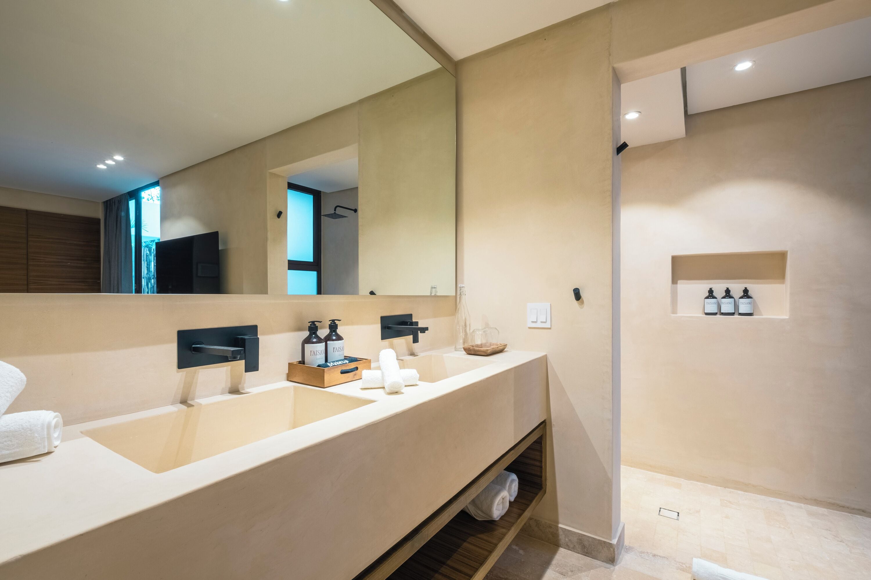 A modern bathroom with a large mirror, dual sinks, and a built-in shelf with toiletries.