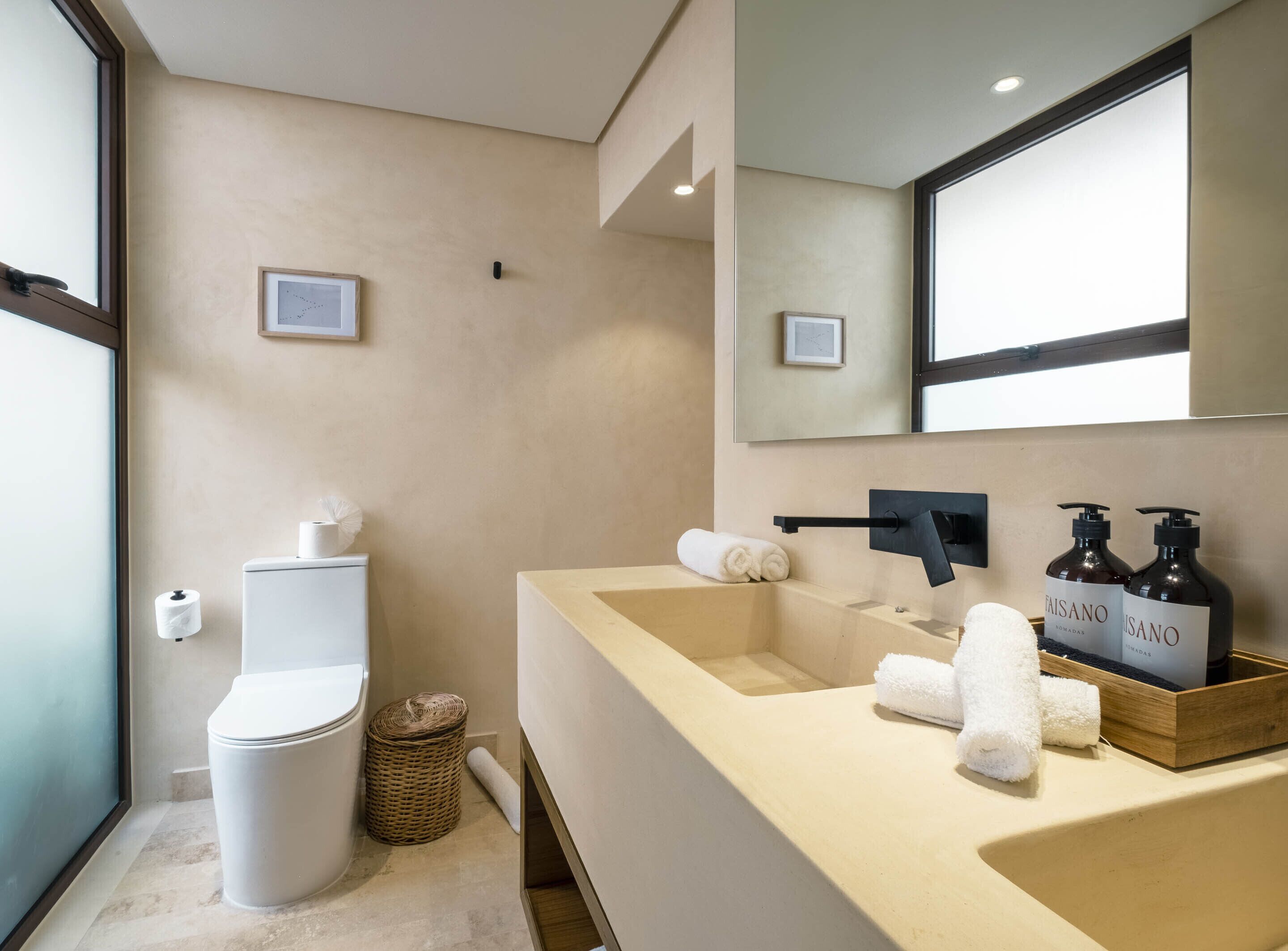 Un baño moderno con inodoro, lavabo y espejo. Hay toallas y artículos de aseo en el lavabo.
