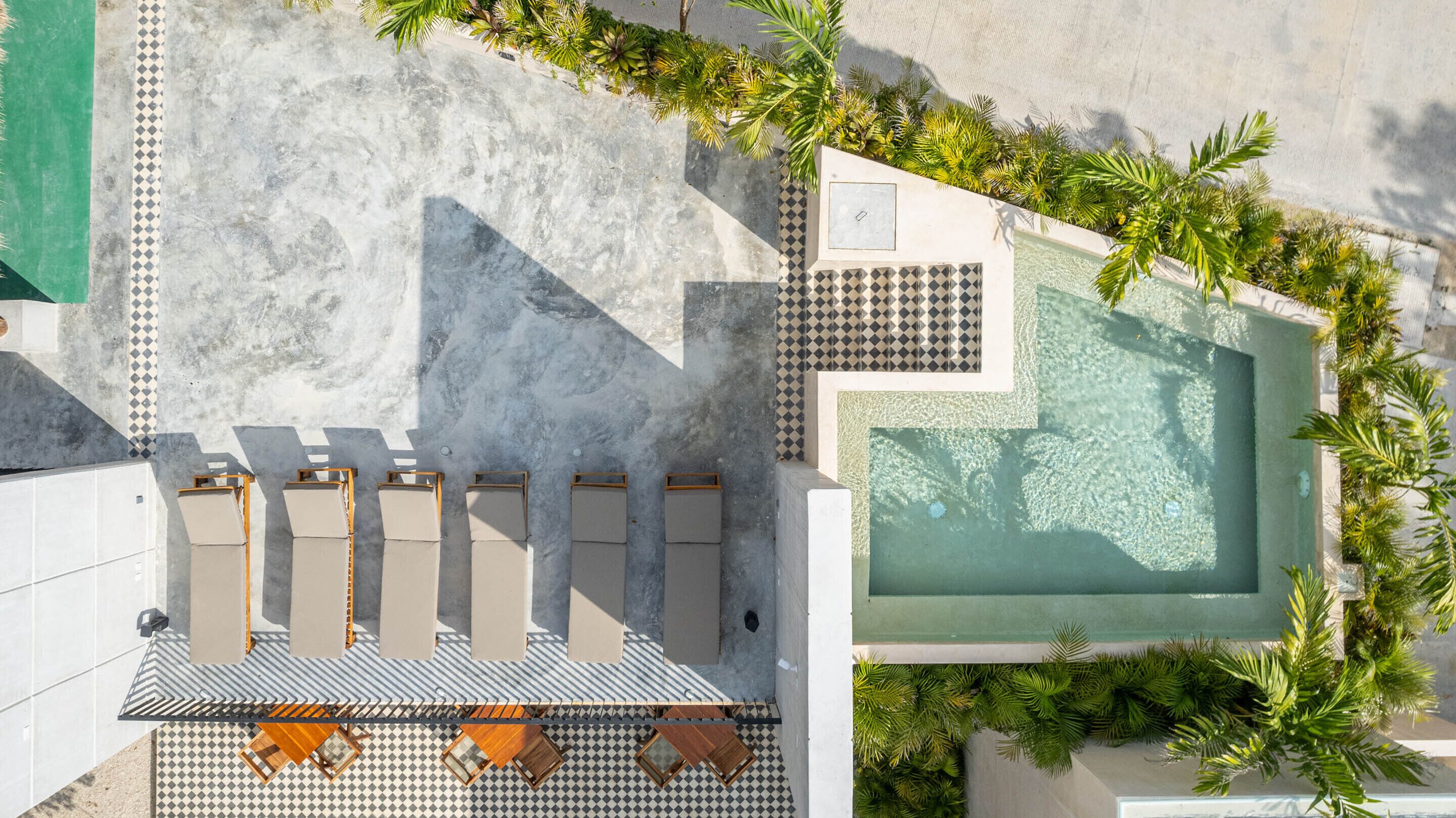 An aerial view of a resort with a swimming pool, lounge chairs, and palm trees.