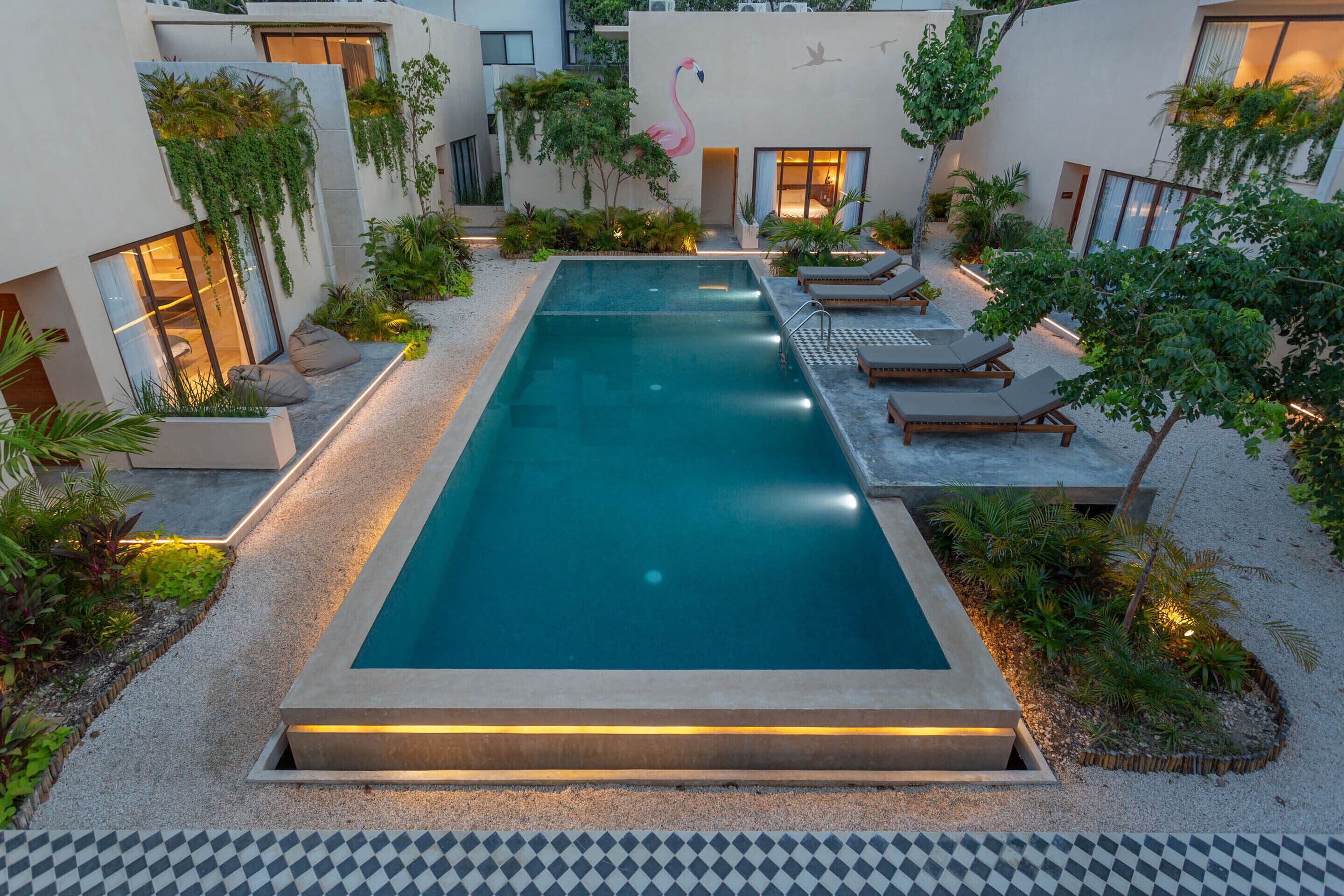 A rectangular swimming pool surrounded by lounge chairs and plants, with a modern architectural design and a flamingo mural on the wall.