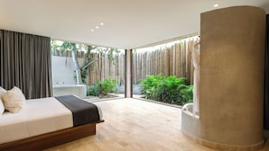 A modern bedroom with a large bed, a curved column, and a view of a garden through large windows.