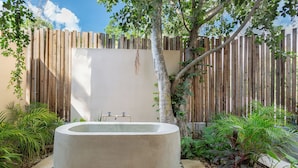 A concrete bathtub in a garden with a wooden fence and plants.