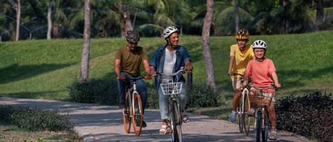 Cuatro personas andando en bicicleta por un camino pavimentado rodeado de follaje.