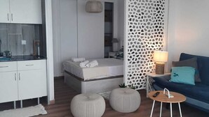 Un espace de vie moderne comprenant un coin cuisine, un canapé, un coin repas et une chambre.