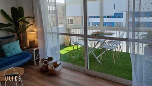Un salon moderne doté d’une grande porte-fenêtre coulissante qui donne sur un espace extérieur avec une pelouse verdoyante et un bâtiment blanc en arrière-plan.