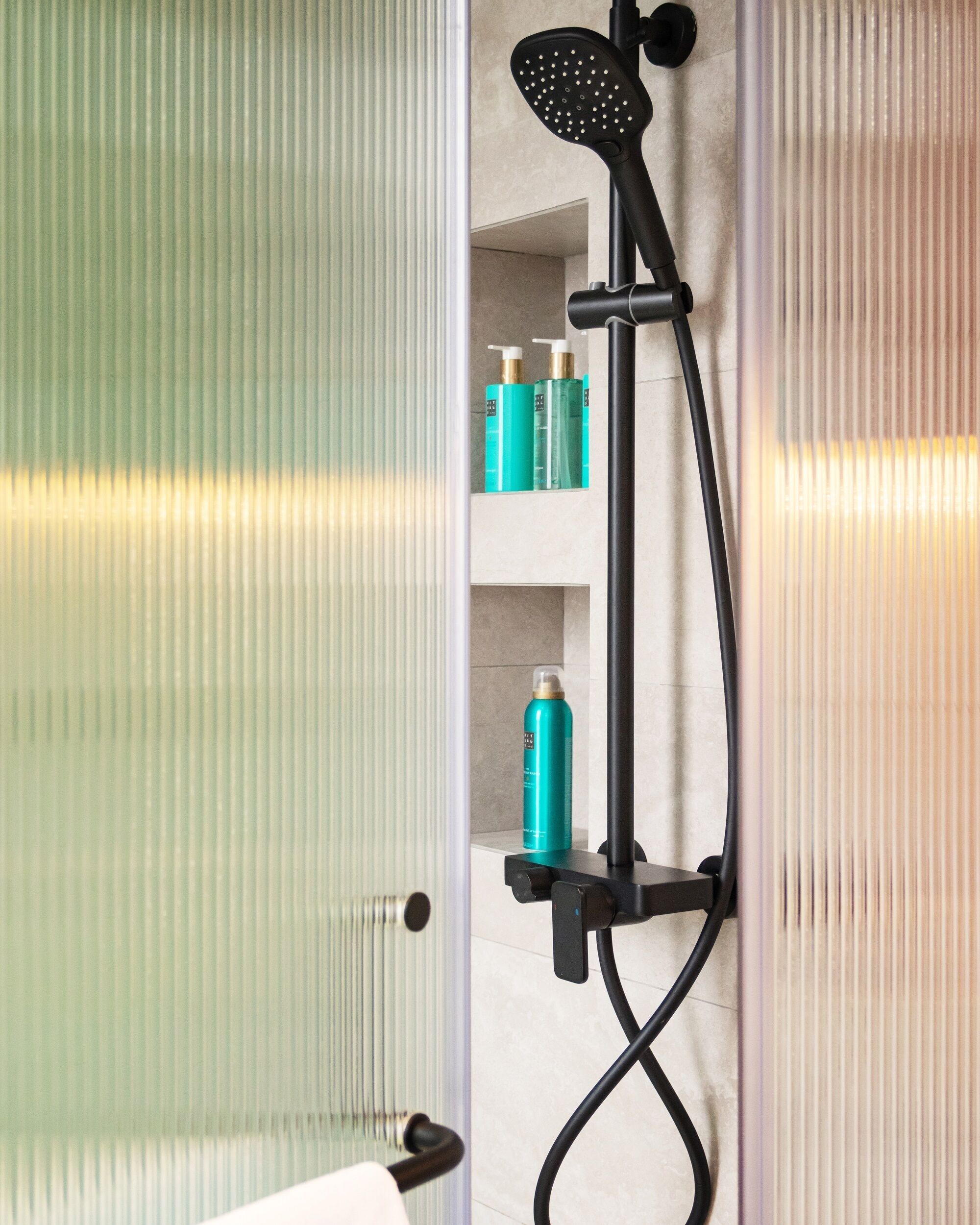 A bathroom with a glass shower enclosure, a handheld showerhead, and shelves with toiletries.