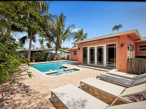 A backyard with a swimming pool, lounge chairs, and palm trees.