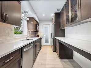 A modern kitchen with dark cabinetry, a white countertop, and a tiled floor.