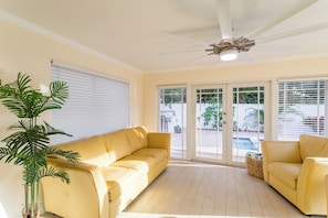 Une pièce avec un canapé jaune, un ventilateur de plafond et une vue sur une piscine, visible à travers des portes vitrées.
