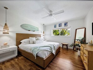 Une chambre à coucher comprenant un lit, une table de chevet, une commode, un ventilateur de plafond, une fenêtre et une décoration sur le thème du surf.