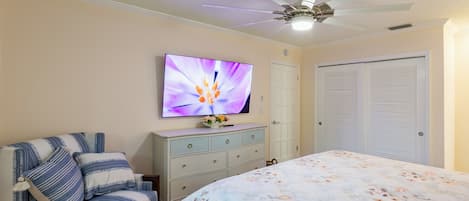 Un dormitorio con una cama, televisión montada en la pared, ventilador de techo y armario.