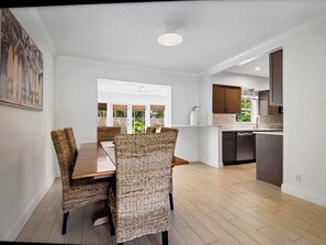 A modern kitchen with dark cabinets, a central island, and a dining area with wicker chairs and a wooden table.