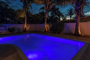 Une piscine à bordures courbes, entourée d’une clôture en bois et de palmiers.
