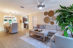A spacious living room with a ceiling fan, a dining area with a chandelier, and a kitchen in the background.