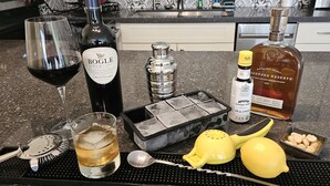 A kitchen counter with a wine bottle, a bottle of bourbon, a glass of wine, a cocktail shaker, a lemon, and a tray with a spoon and a brush. - Scandia 203 - Sleeps 6, Full Kitchen, Free Parking, and 1 Block to the Beach (Honolulu)