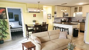 A living room with a sofa, coffee table, and a dining area with chairs and a table. - Scandia 203 - Sleeps 6, Full Kitchen, Free Parking, and 1 Block to the Beach (Honolulu)