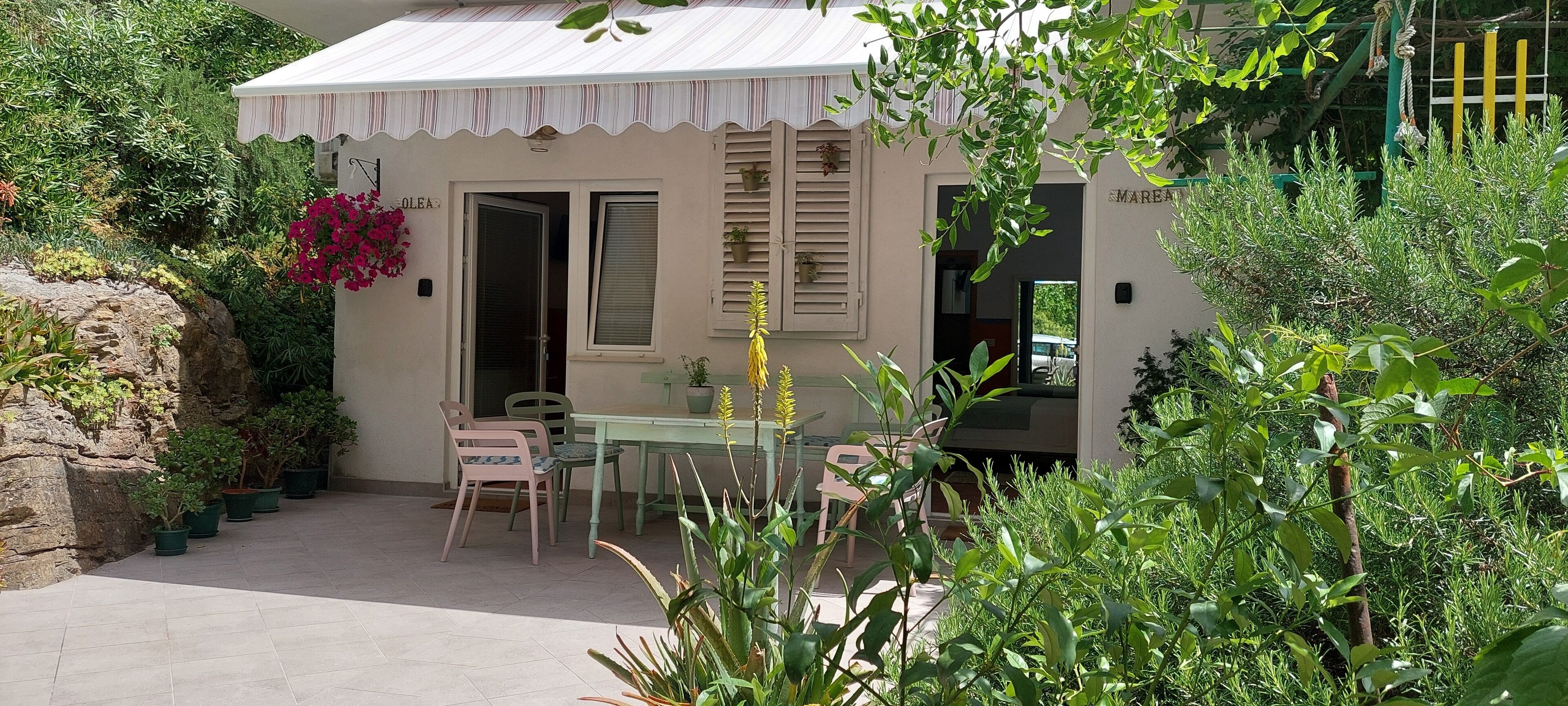 A small building with a white exterior, a covered patio with chairs, and potted plants.