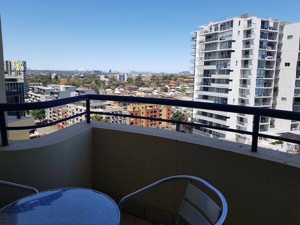 Un balcón con una mesa y sillas, con vistas a un paisaje urbano con varios edificios.