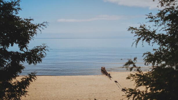 A beach with calm water and a wooden structure in the distance. - Little Blue Cottage - wooded getaway, near beaches and towns (Benton Harbor)